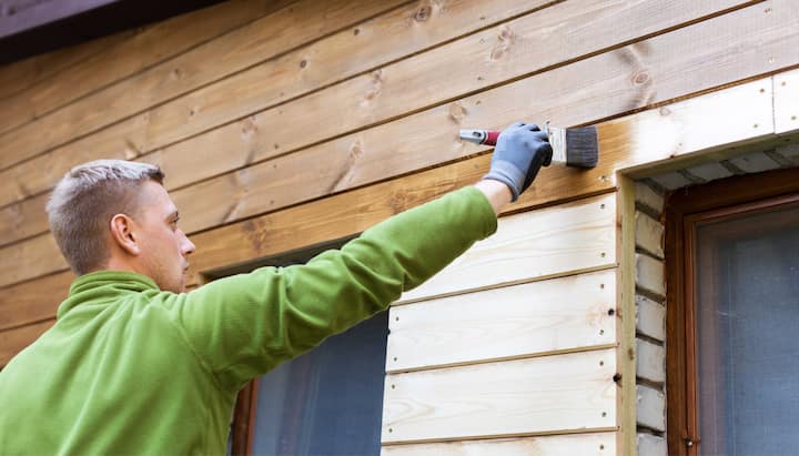 A professional painter using a long-handled brush to apply paint to the exterior of a house in Charlotte.